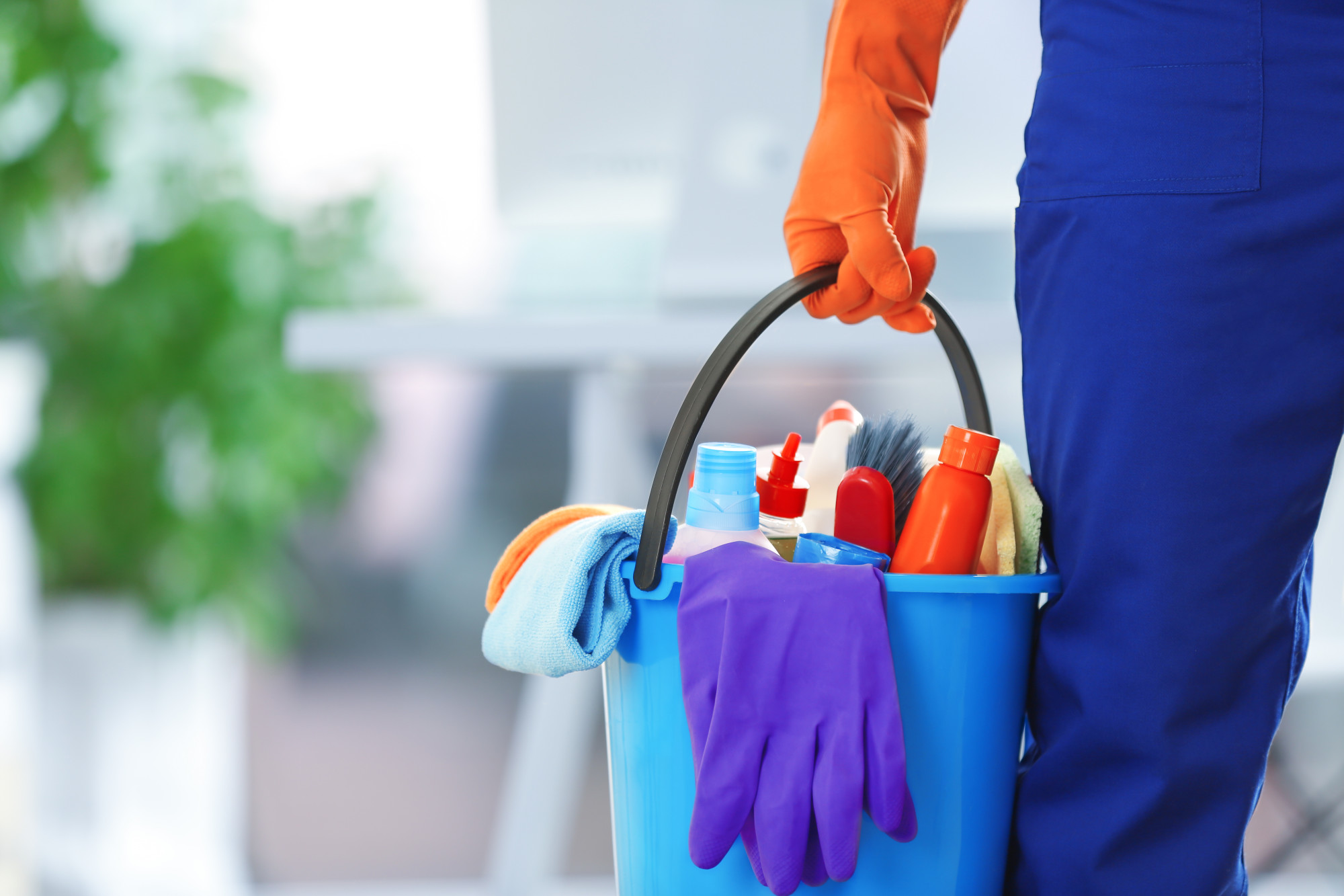 A person in uniform holding a bucket of cleaning supplies in a bright office