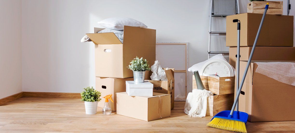 Moving boxes stacked in an empty room with cleaning supplies nearby
